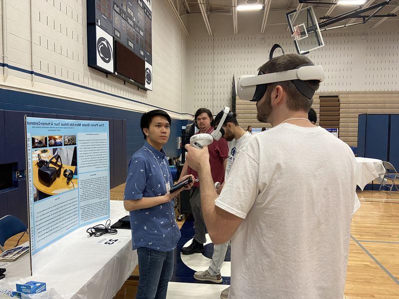 A student wears a virtual reality headset while another student looks on.