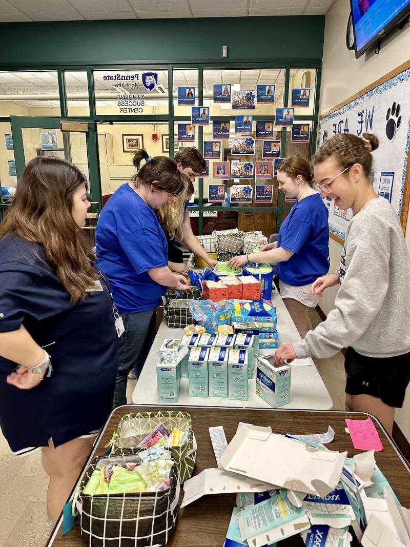 Students stand around a table and look down while preparing baskets