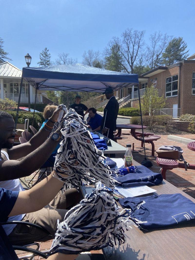 Arms wave pom poms while Chancellor Dr. A stands in the distance under a sun tent.